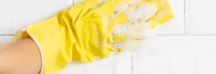 Hand in Gummihandschuh reinigt Fliesen mit Schwamm.